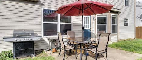 En terrasse med grill, bord, stole og en rød parasol.