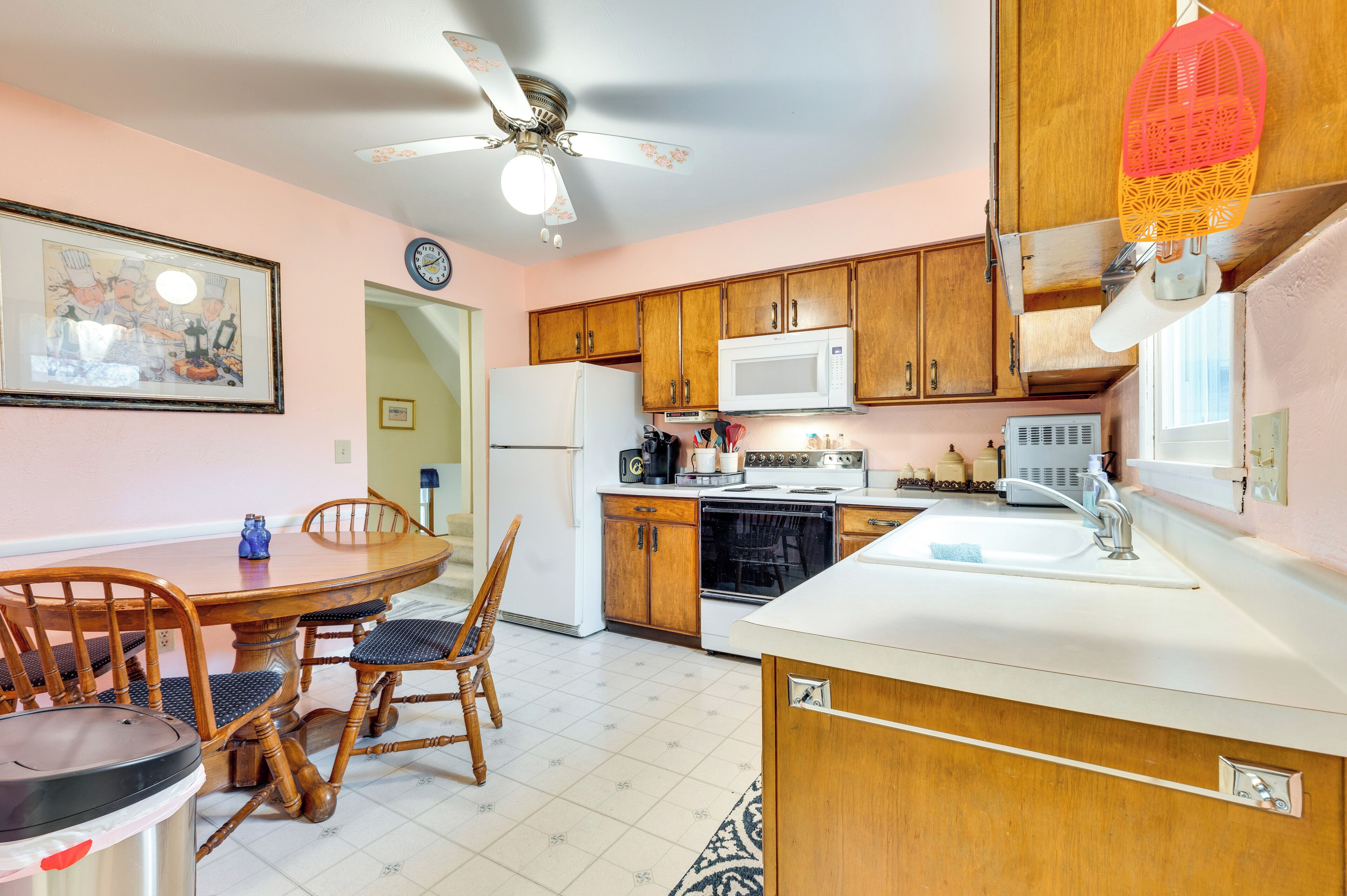 Una cocina con gabinetes de madera, microondas, refrigerador, mesa de comedor con sillas y ventilador de techo.