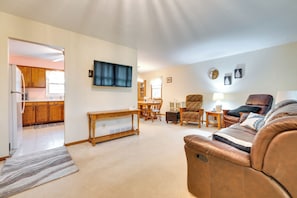 A living room with a brown leather sofa, a wooden coffee table, and a TV mounted on the wall. There is a kitchen visible through an open doorway. - Clear Lake Vacation Home Rental - Pet Friendly! (Clear Lake)