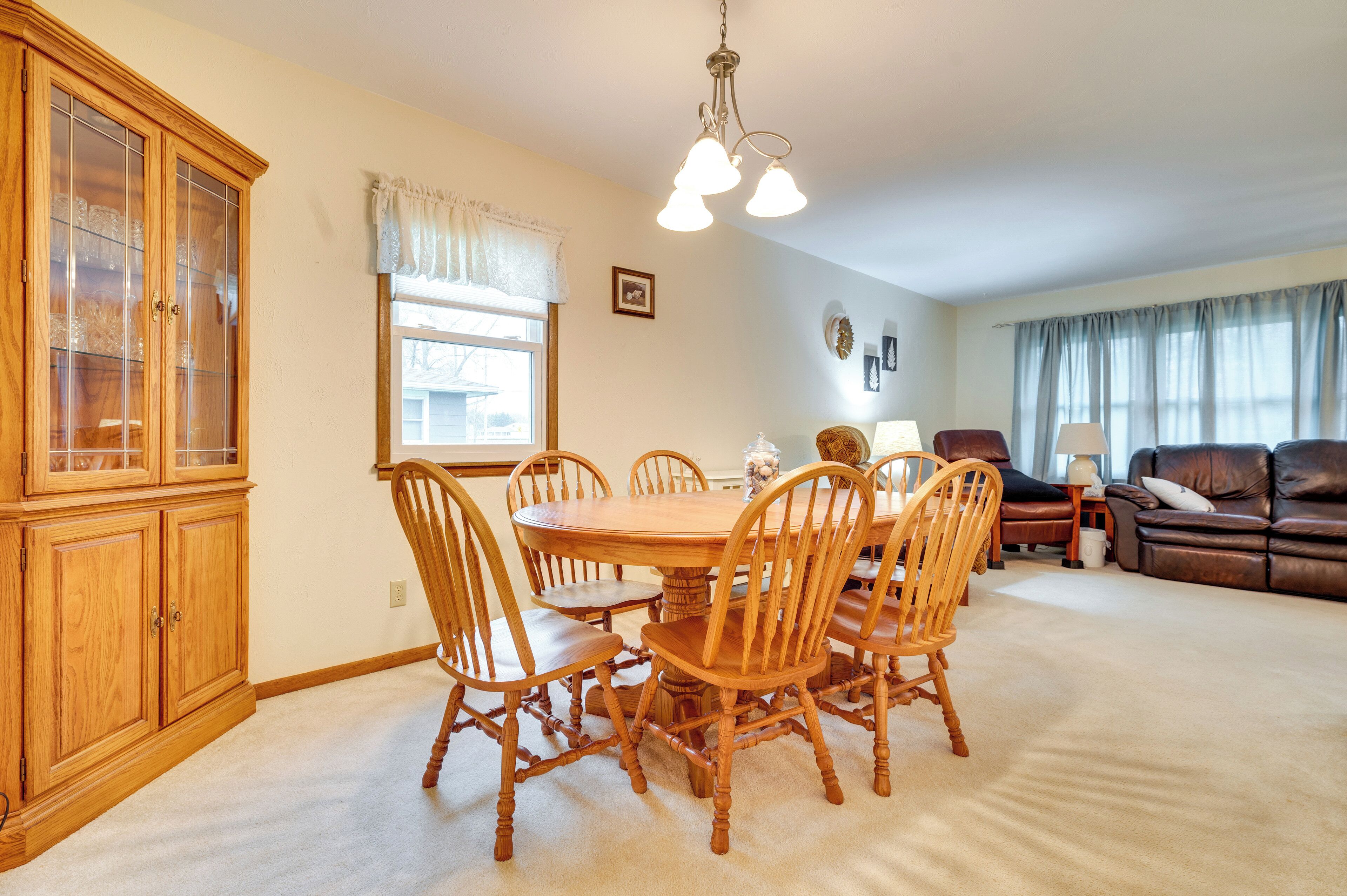 A dining area with a wooden table and chairs, a cabinet, and a window with curtains.
