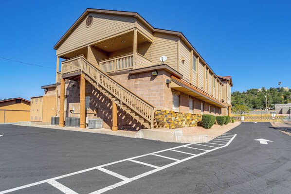 A two-story building with a balcony on the upper floor, a staircase leading to the entrance, and a parking lot in front.