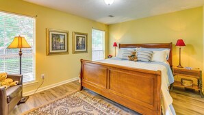 A bedroom with a wooden bed, two bedside lamps, a rug, and two framed pictures on the wall. - 2 Mi to Uca: Group Getaway w/ Private Yard! (Conway)