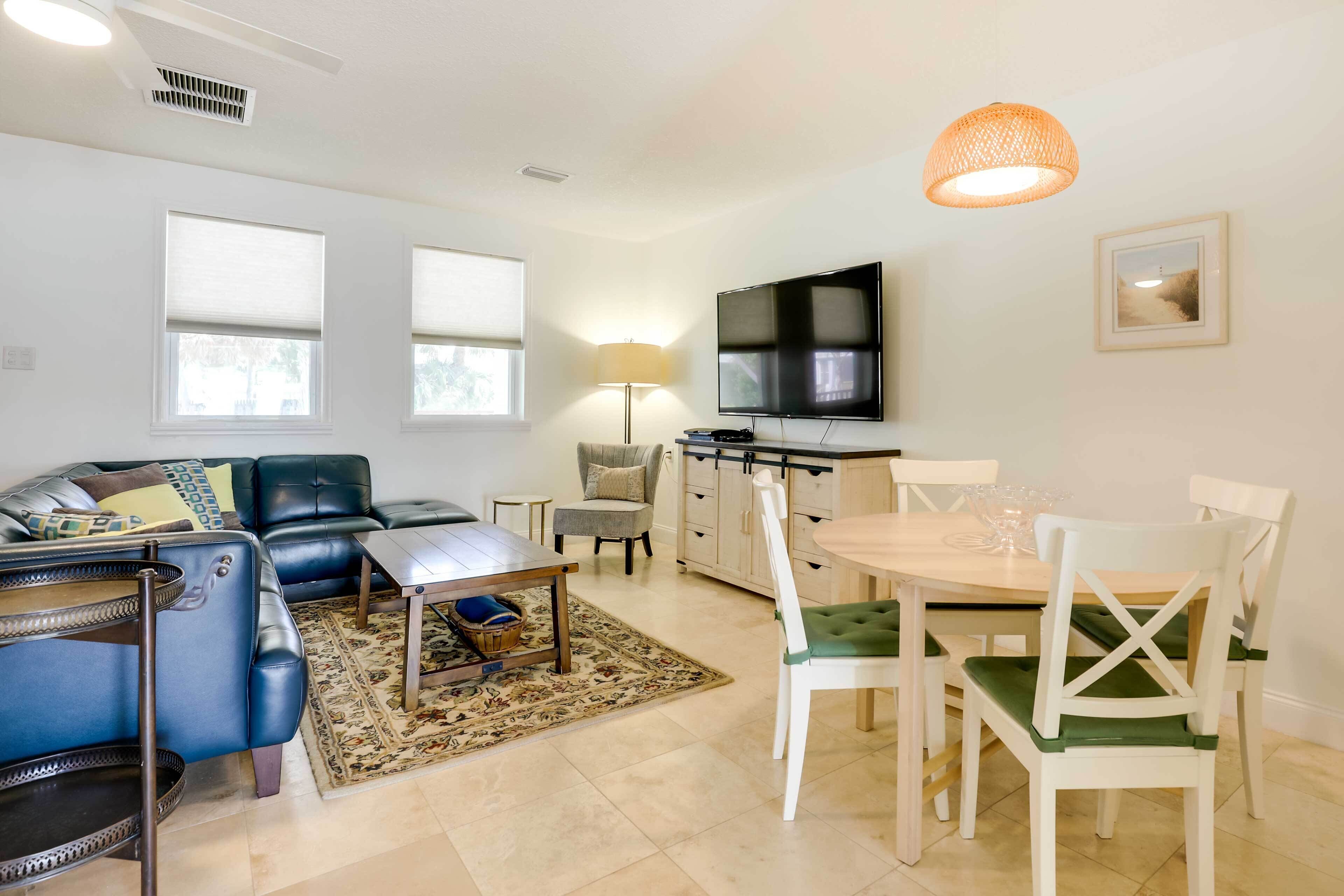 A living room with a sofa, coffee table, and TV. There is a dining area with a table and chairs.