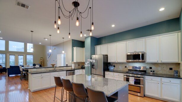 A modern kitchen with white cabinets, a large island with bar stools, stainless steel appliances, and pendant lighting. - Houston Townhome By George Brown Convention Center (Houston)