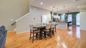 A modern kitchen with a central island, wooden flooring, and a dining area with a table and chairs. - Houston Townhome By George Brown Convention Center (Houston)
