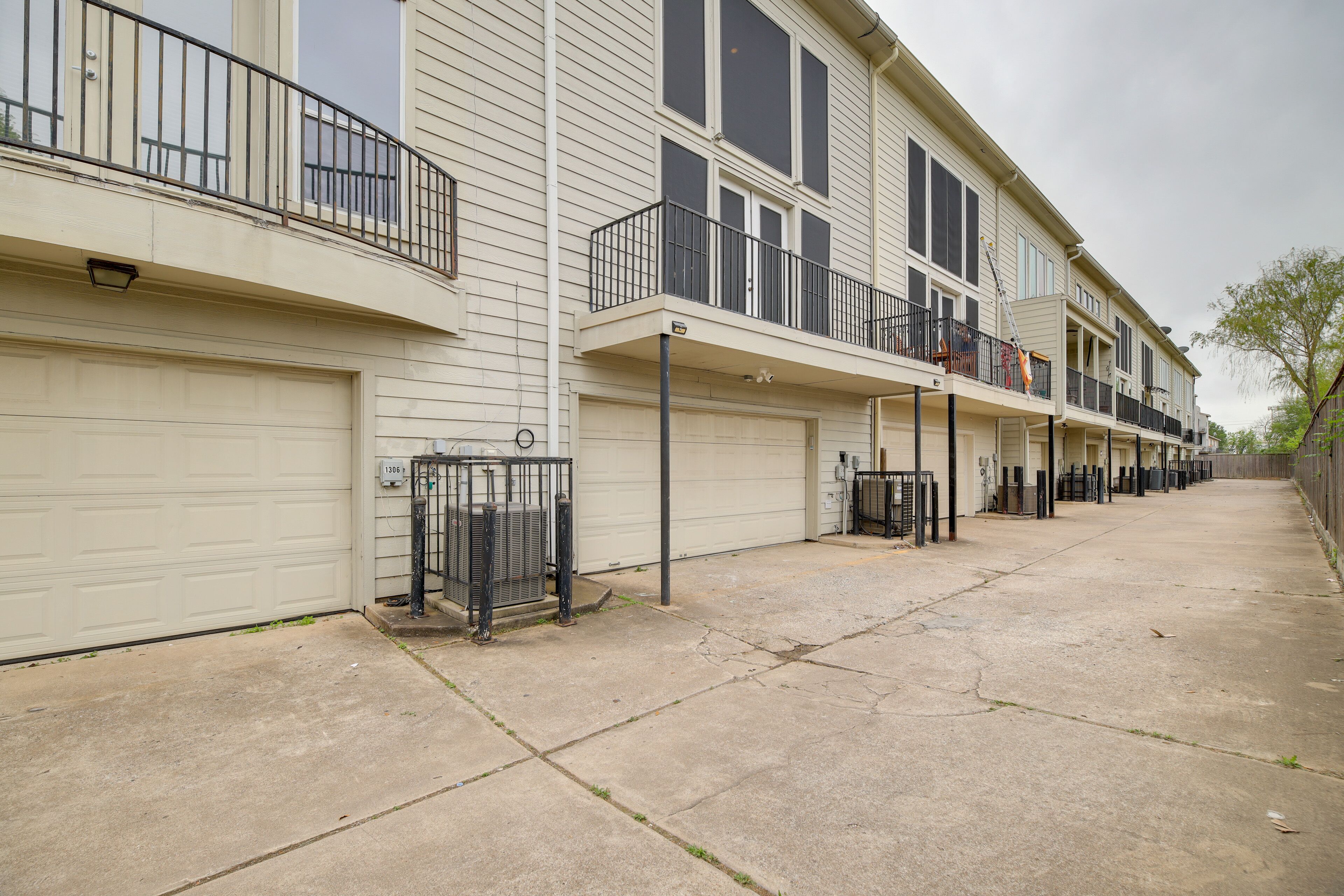 A row of townhouses with attached garages, a concrete driveway, and a metal fence.