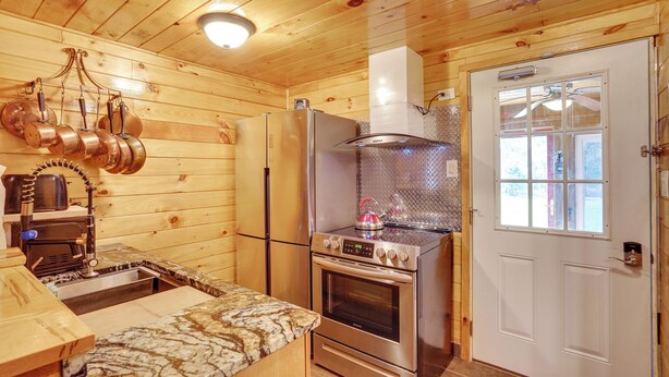 Un intérieur en bois avec un coin cuisine doté d’appareils électroménagers en acier inoxydable, d’un plan de travail en marbre et d’une fenêtre offrant une vue agréable.