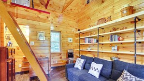 L’intérieur d’un chalet accueillant, avec un escalier en bois, un canapé agrémenté de coussins et des étagères remplies de divers objets.