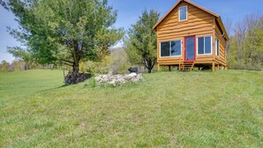 Une cabane en bois avec une porte rouge, entourée d’un champ verdoyant et d’arbres.