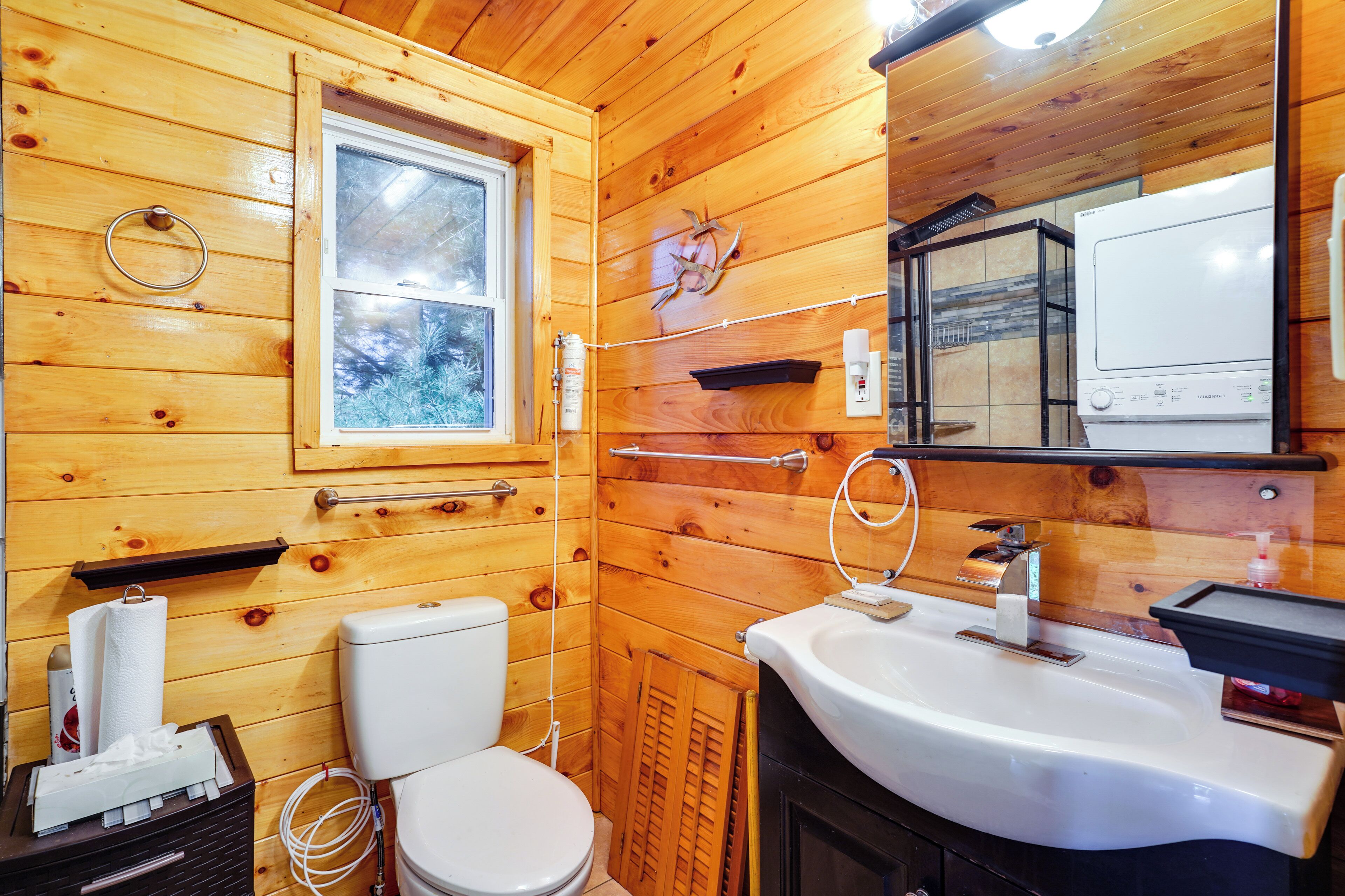 A wooden cabin bathroom with a toilet, sink, and window.