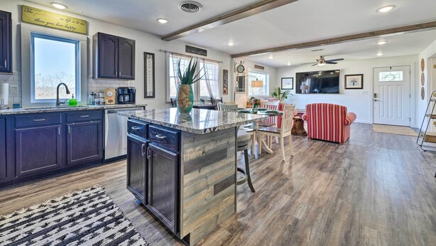 A modern kitchen with dark cabinets, a large island, and a dining area with a red-striped sofa. - Boho Mountain Home Escape, Walk to Marina! (Mountain Home)