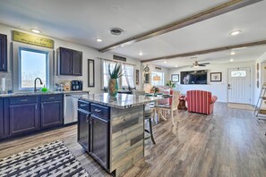 A modern kitchen with dark cabinets, a large island, and a dining area with a red-striped sofa. - Boho Mountain Home Escape, Walk to Marina! (Mountain Home)