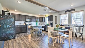 A modern kitchen with dark cabinets, a central island with stools, and a dining table set for four. - Boho Mountain Home Escape, Walk to Marina! (Mountain Home)