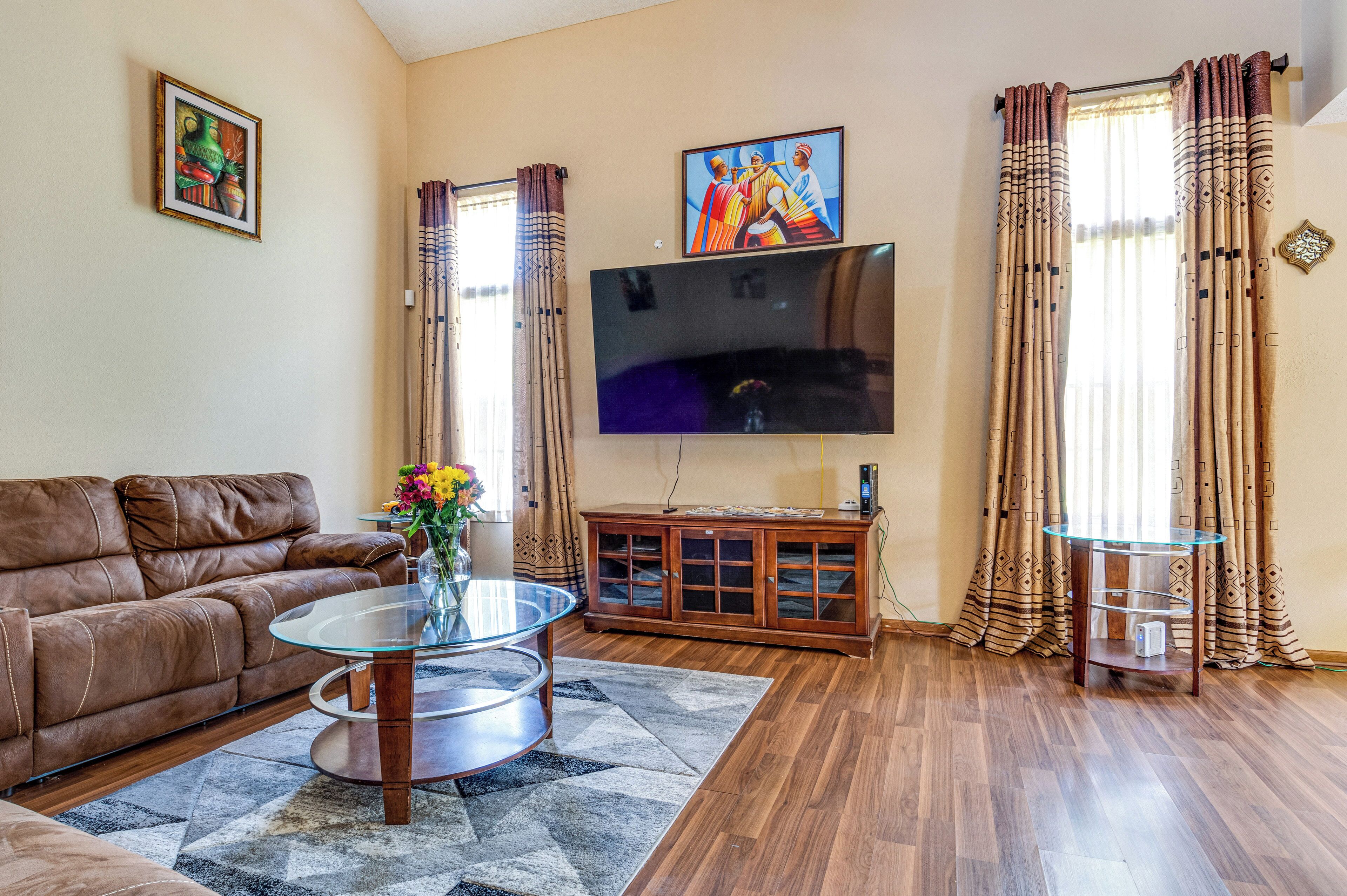 A living room with a brown leather sofa, a glass coffee table, a TV mounted on the wall, and a wooden cabinet.