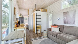 A modern, open-plan living space with a loft area, a kitchen, and a seating area with a sofa and cushions. - Updated Texas Tiny Home Rental on Lake Travis (Spicewood)
