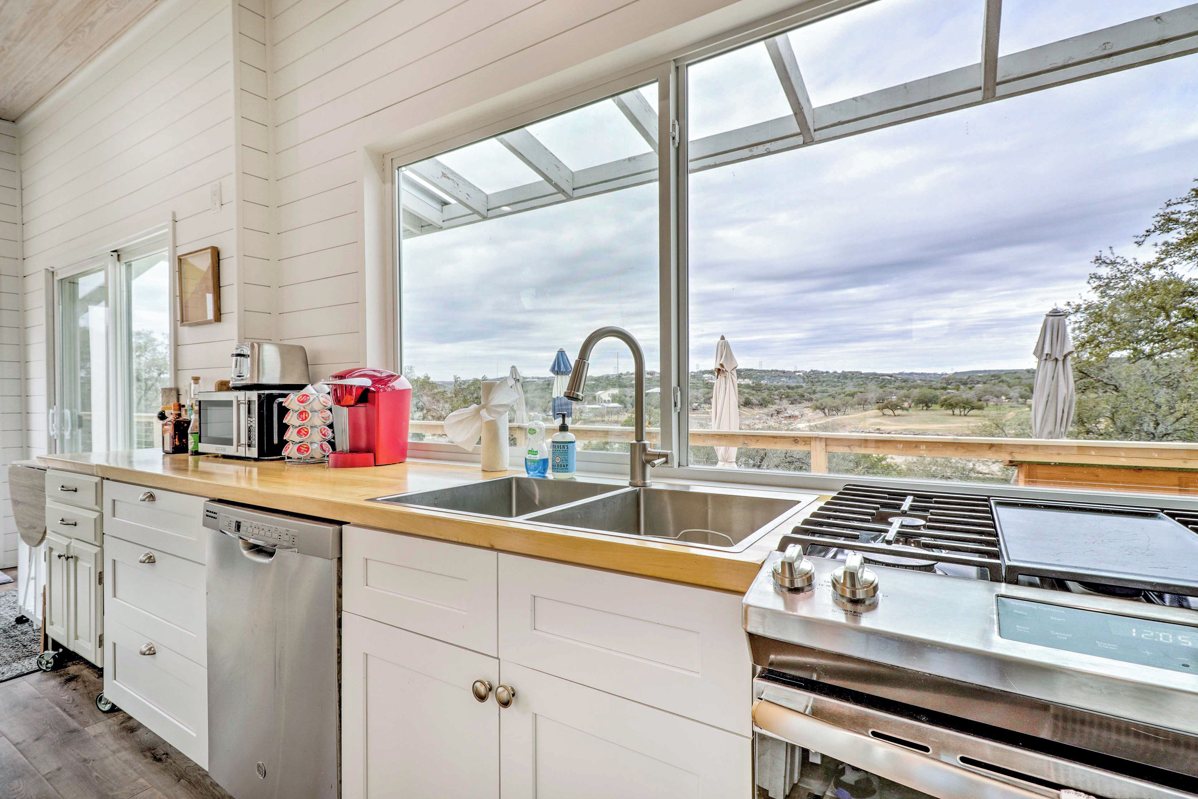 A kitchen with a large window, a sink, a dishwasher, and a stove.