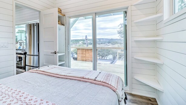 A bedroom with a large bed, a sliding glass door leading to a balcony, and a view of the outside. - Updated Texas Tiny Home Rental on Lake Travis (Spicewood)