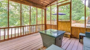 A covered deck with a glass-top table and wicker furniture, overlooking a wooded area. - Lakefront Arkansas Abode - Deck, Grill & Fire Pit (Scranton)