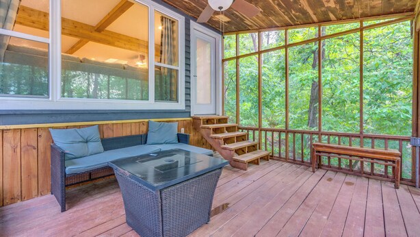A covered deck with a wicker sofa, a glass-top table, and a wooden bench. - Lakefront Arkansas Abode - Deck, Grill & Fire Pit (Scranton)