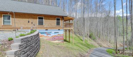 A log cabin with a wooden deck and a colorful mural on the exterior wall.