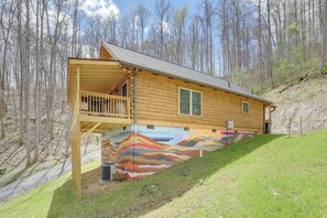 A log cabin with a balcony, surrounded by a forest.
