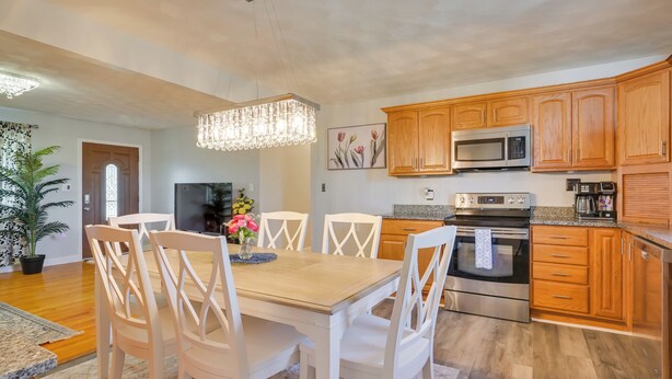 A modern kitchen with wooden cabinets, a stainless steel oven, and a dining area with white chairs and a wooden table. - Deck & Grill: Convenient Home in Hummelstown (Hershey)