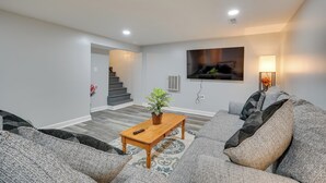 A modern living room with a sofa, a coffee table, and a staircase leading to another level. - Deck & Grill: Convenient Home in Hummelstown (Hershey)