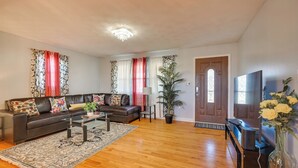 A living room with a dark leather sofa, a glass coffee table, a potted plant, and a television on a stand. - Deck & Grill: Convenient Home in Hummelstown (Hershey)