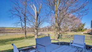 An outdoor patio with white metal furniture, including a table and chairs, set against a backdrop of leafless trees and a clear blue sky. - Deck & Grill: Convenient Home in Hummelstown (Hershey)