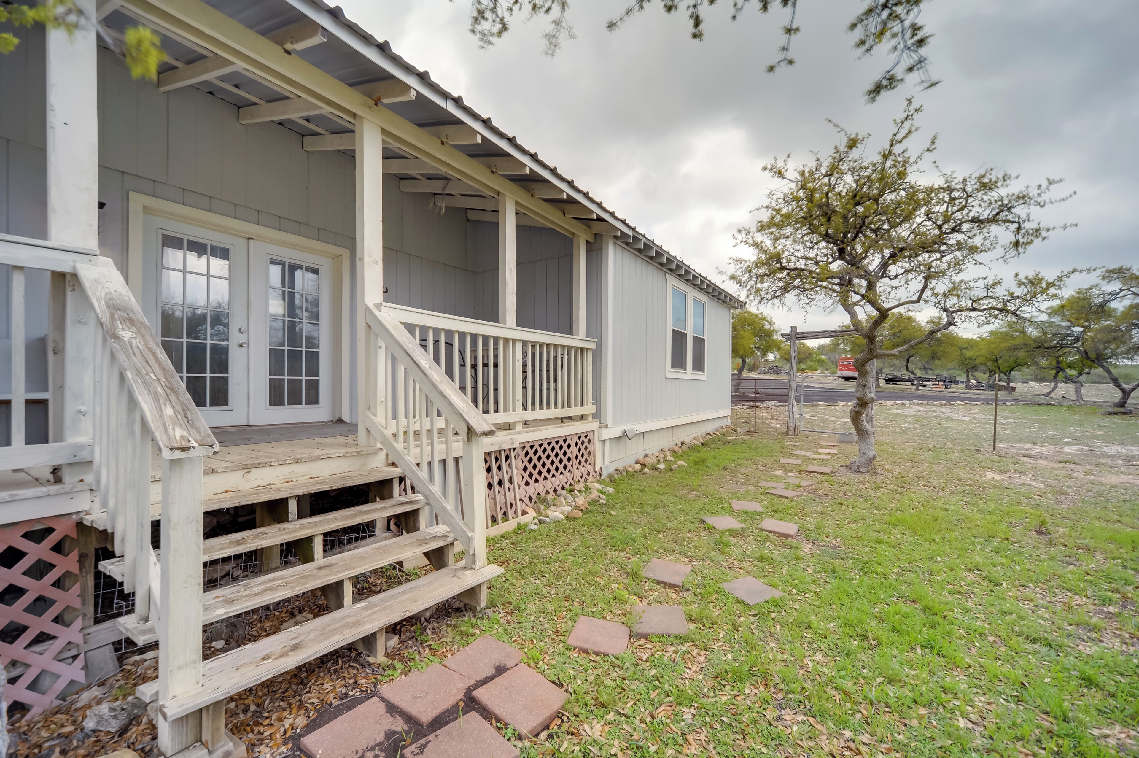 A single-story house with a front porch, a small staircase, and a tree in the yard.