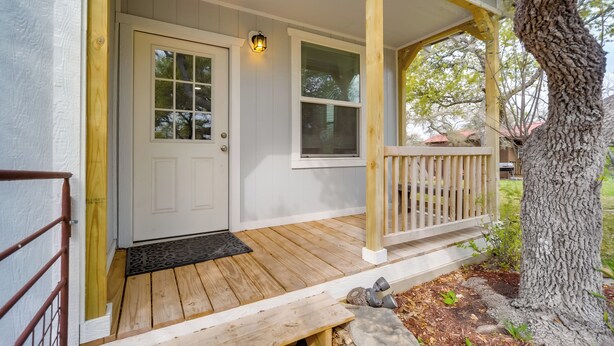 Une véranda en bois avec une porte blanche et une fenêtre, un banc et un arbre.