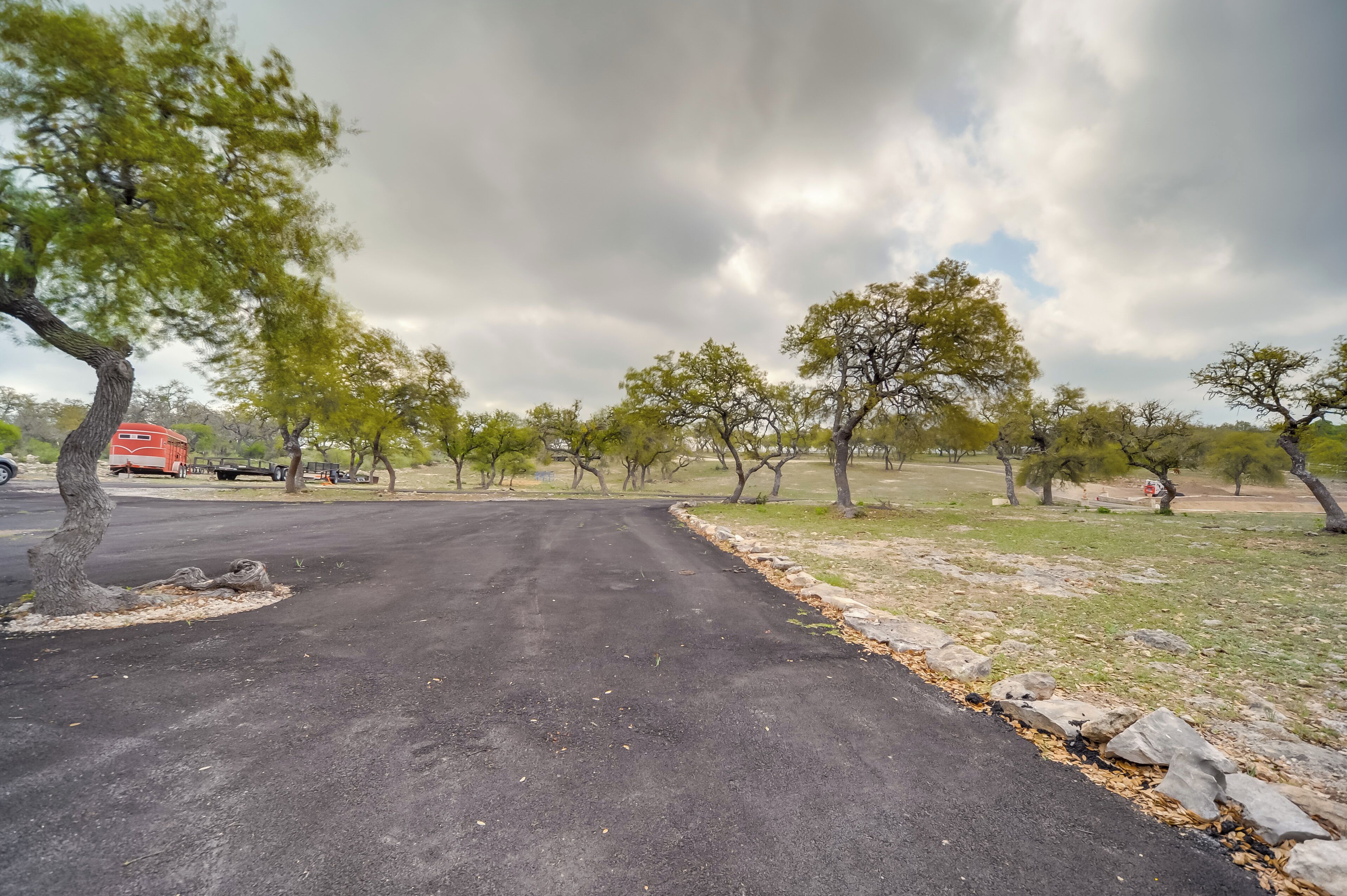 A paved road with trees on both sides, a red vehicle in the distance, and a cloudy sky.