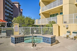 A hot tub area with a tiled pool, white railings, and lounge chairs.