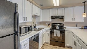 Una cocina con armarios blancos, un refrigerador de acero inoxidable, un microondas, un lavavajillas, un horno y un fregadero.