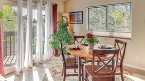 Un comedor con una mesa, sillas, una planta en maceta y un ventanal con vistas a árboles.