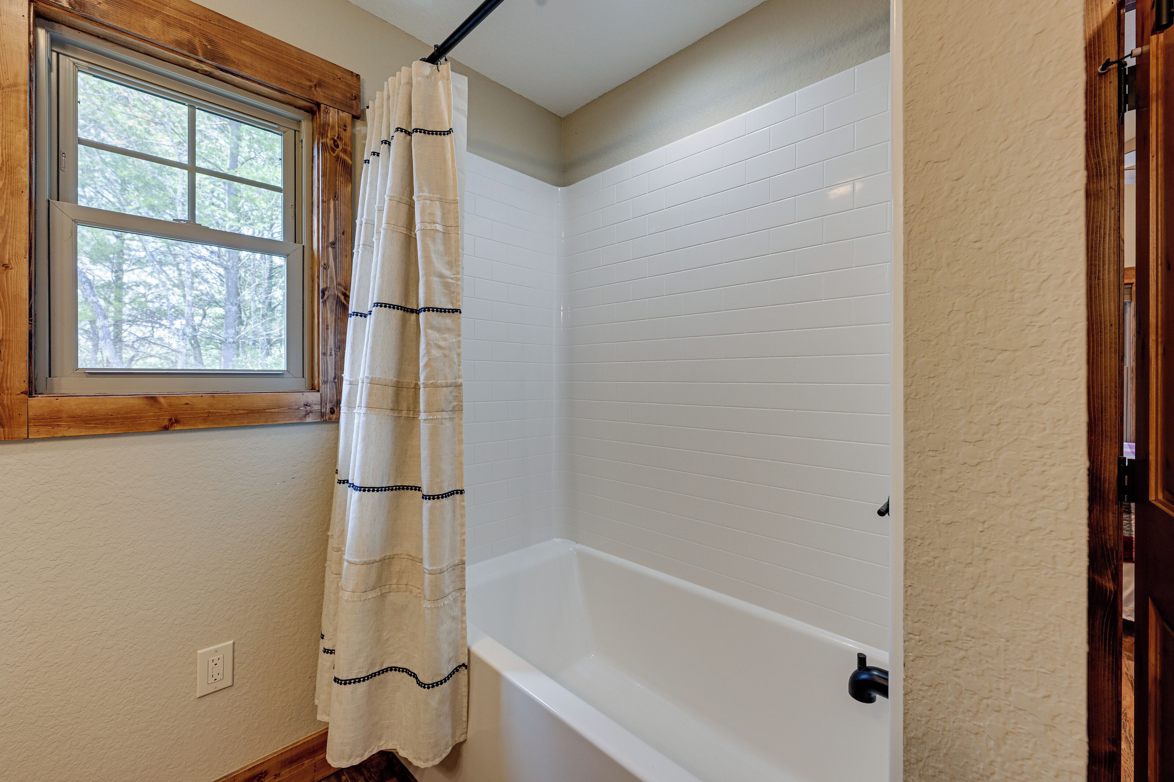 A bathroom with a bathtub, a window with a wooden frame, and a shower curtain.