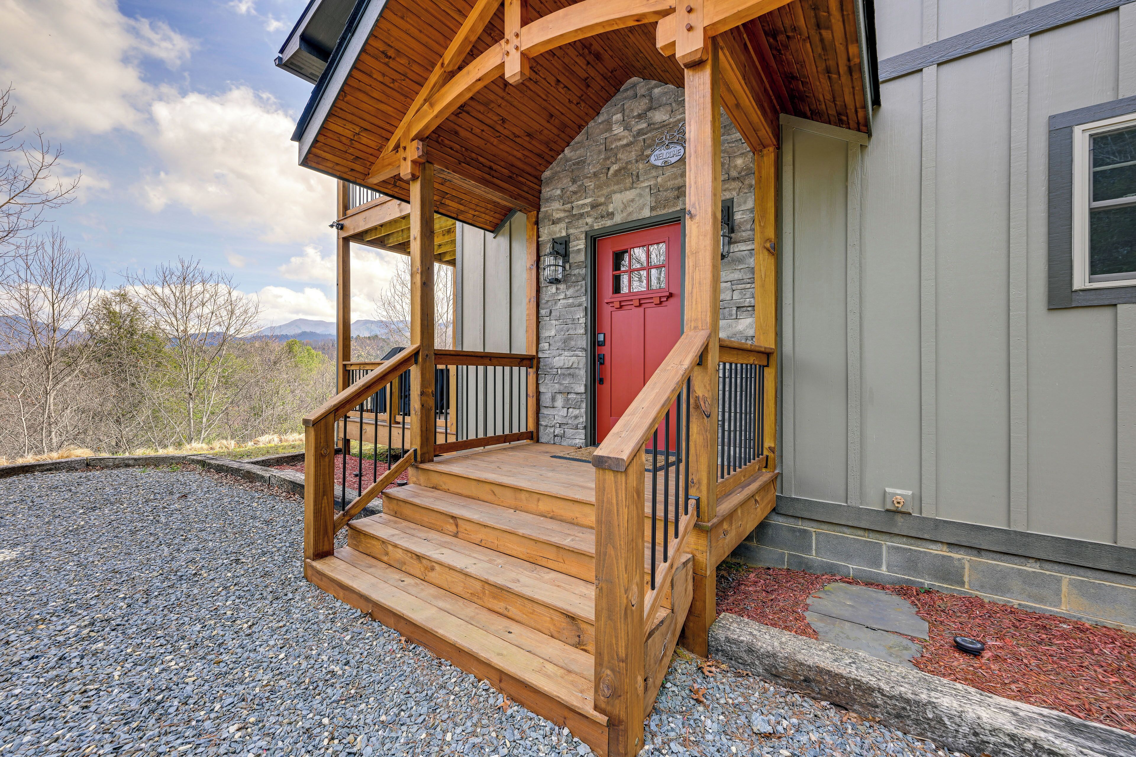 A wooden porch with a red door, stone wall, and a view of mountains.