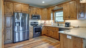 A kitchen with wooden cabinets, stainless steel appliances, a granite countertop, and a window providing natural light. - Smoky Mountain Cabin Rental: Game Room, Fire Pit! (Andrews)