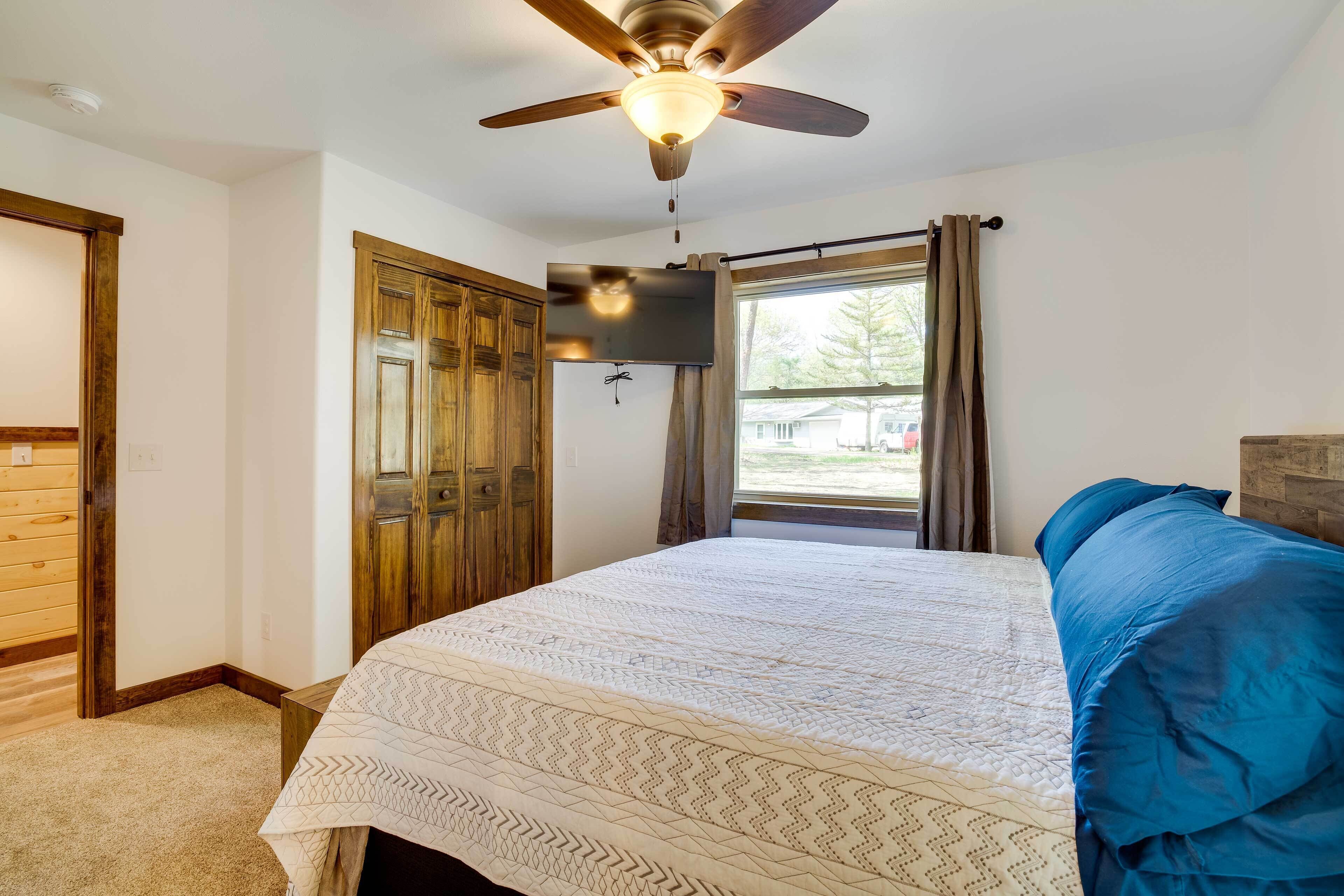 A bedroom with a bed, a ceiling fan, a window with curtains, and wooden doors.