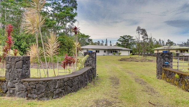 A stone pathway leading to a house with a stone wall on one side and a grassy area with trees and plants. - Paradise Park Vacation Rental ~ 4 Mi to Shoreline! (Keaau)