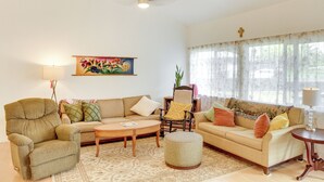 A living room with a sofa, armchair, ottoman, and a painting on the wall. - Paradise Park Vacation Rental ~ 4 Mi to Shoreline! (Keaau)