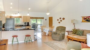A spacious living area with a sofa, armchair, and ottoman, a dining table with chairs, a kitchen with a refrigerator and stove, and a small bar area with stools. - Paradise Park Vacation Rental ~ 4 Mi to Shoreline! (Keaau)