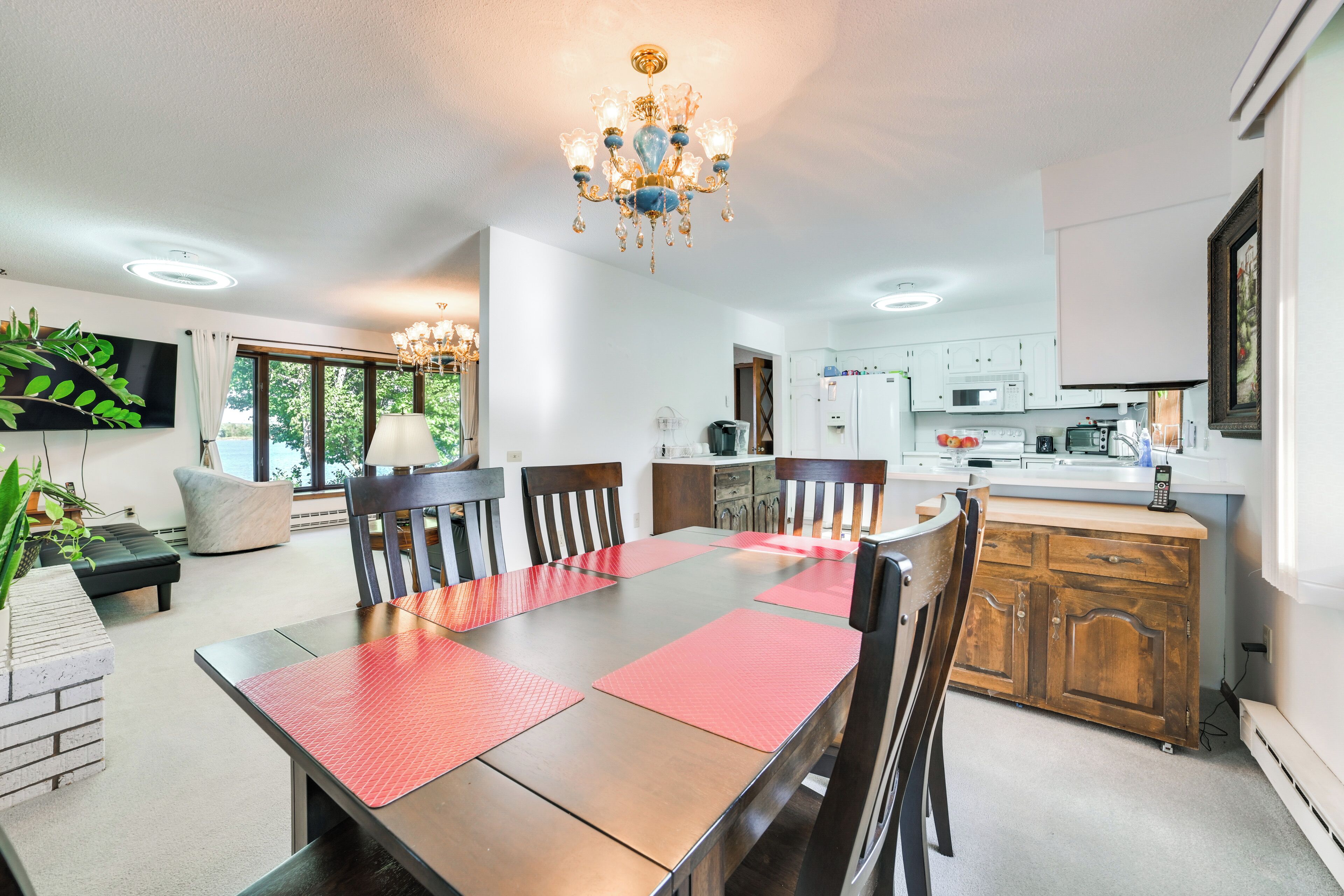 A dining area with a wooden table, red placemats, and chairs. There is a chandelier above the table.