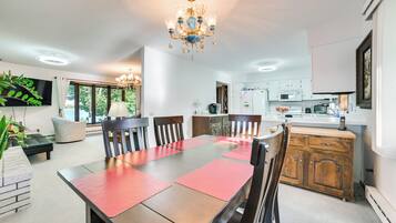 A dining area with a wooden table, red placemats, and chairs. There is a chandelier above the table.