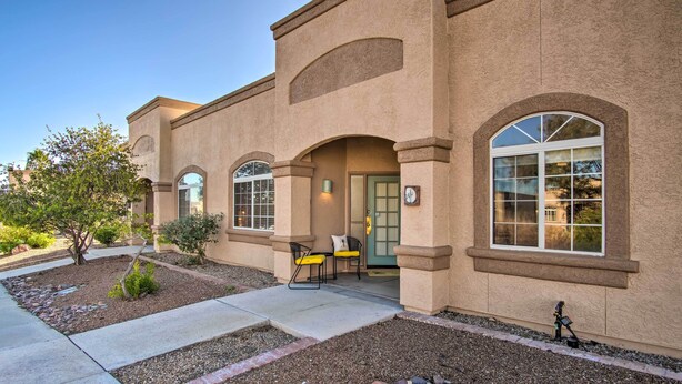 A building with a stucco exterior, arched windows, and a small patio area with chairs and a table. - Green Valley Studio in 55+ Community! (Green Valley)