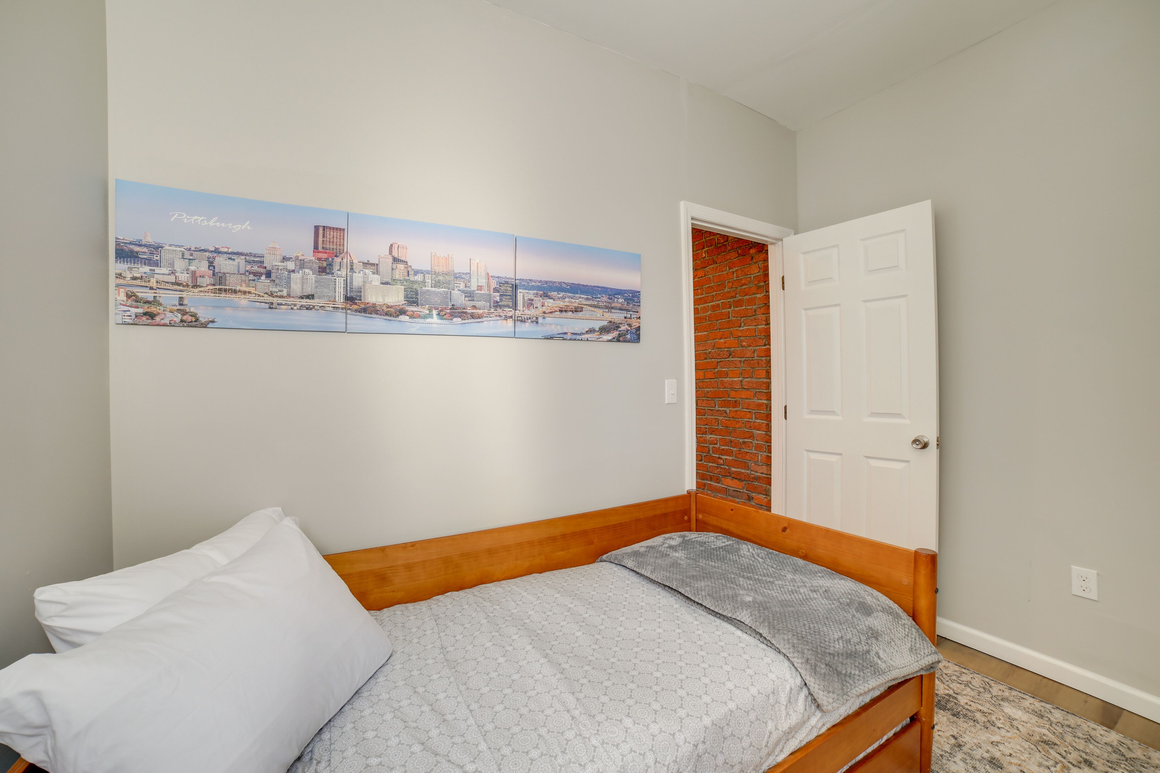 A bedroom with a bed, a white door, and a cityscape painting on the wall.