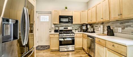 A modern kitchen with stainless steel appliances, wooden cabinets, and a tiled backsplash.
