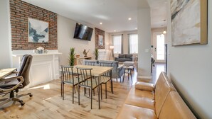 A modern living room with a dining area, a brick accent wall, a flat-screen TV, and a large abstract painting. - Pittsburgh Townhome: 1 Mi to Downtown (Pittsburgh)