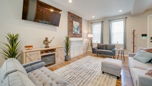 A modern living room with a fireplace, grey sofas, and a flat-screen TV mounted on the wall. - Pittsburgh Townhome: 1 Mi to Downtown (Pittsburgh)