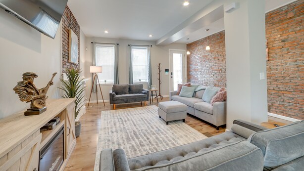 A modern living room with a fireplace, grey sofas, a coffee table, and a brick accent wall. - Pittsburgh Townhome: 1 Mi to Downtown (Pittsburgh)